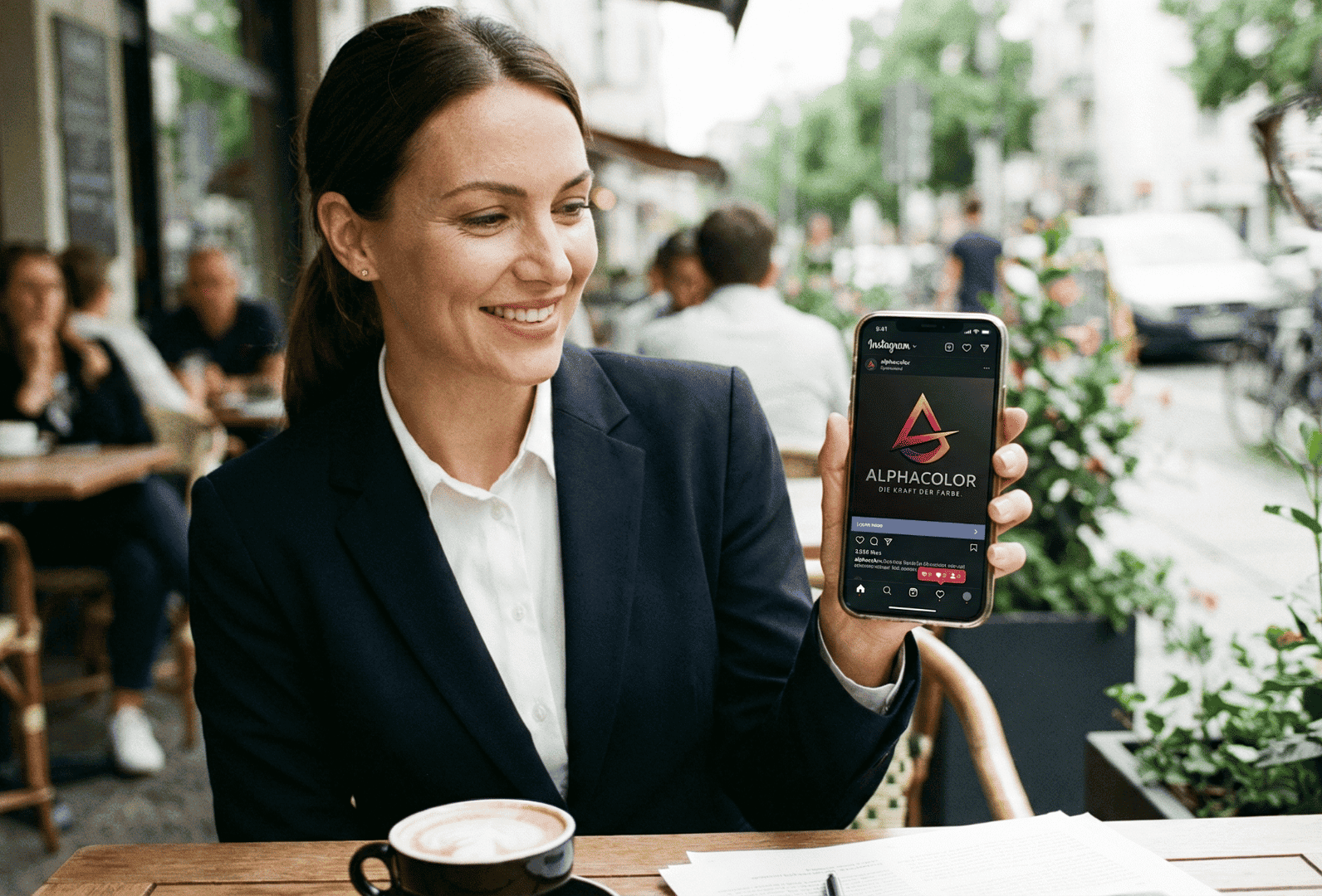 Geschäftsfrau präsentiert Alphacolor auf Smartphone in urbanem Café